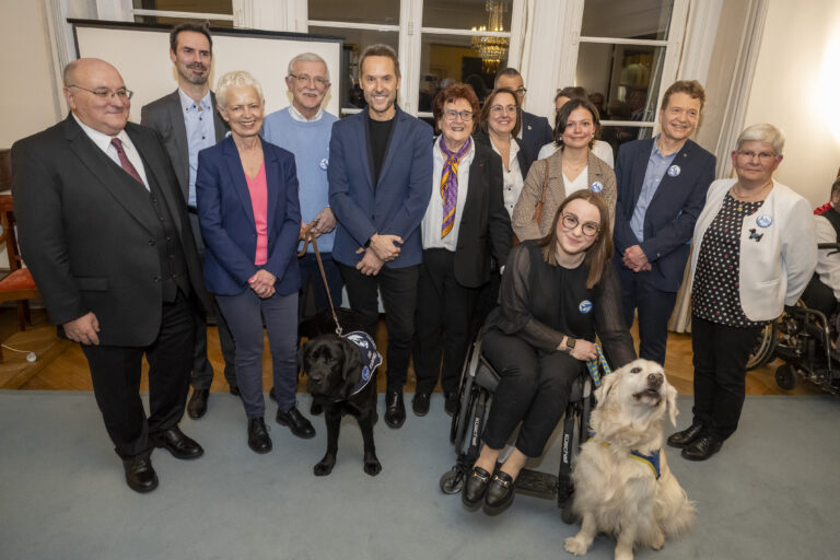 Décoration par Brigitte Klinket, Questeure, de TOBY 500e Chien d’Assistance à mission collective de l’Association Handi’Chiens présidée par M. Robert Kohler, à l'Assemblée nationale le 26 mars 2025.